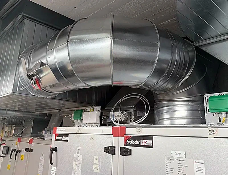 Ventilationsrum med rör, kanaler och teknisk utrustning vid fönster.